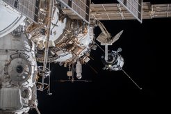 A Soyuz capsule approaches the ISS, in the foreground the rod-shaped Icarus antenna can be seen.